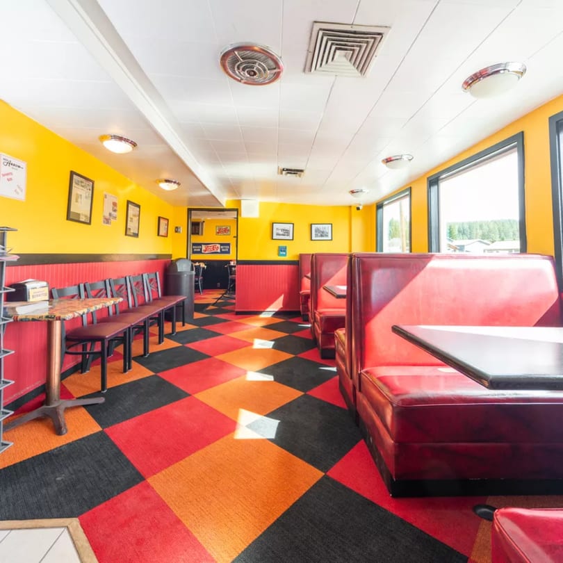 A diner interior with red booths, yellow walls, and a checkered red, orange, and black floor.