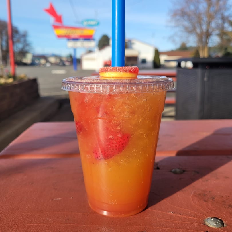 A vibrant orange and red drink with strawberries, a blue straw, and a candy garnish on a table.