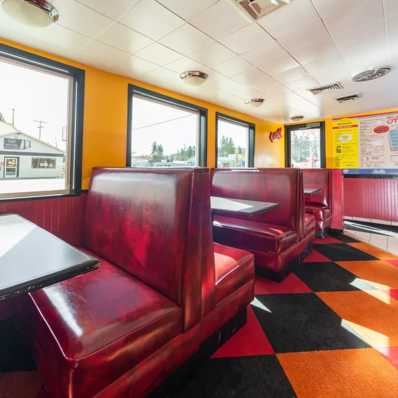 Interior of a diner with red booths, yellow walls, and a black, orange, and red checkered floor.